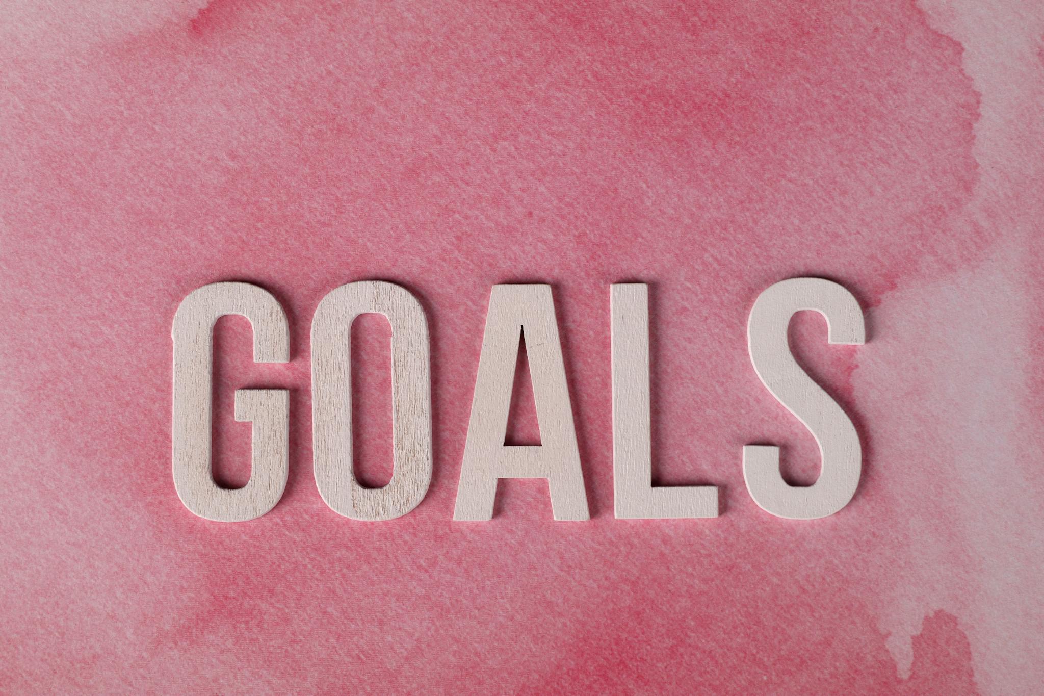 Motivational word 'GOALS' on a pink watercolor background for inspiration.
